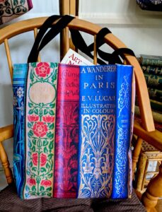 a book tote bag with art nouveau old book spines in rich primary colours as a gift for bibliophiles.